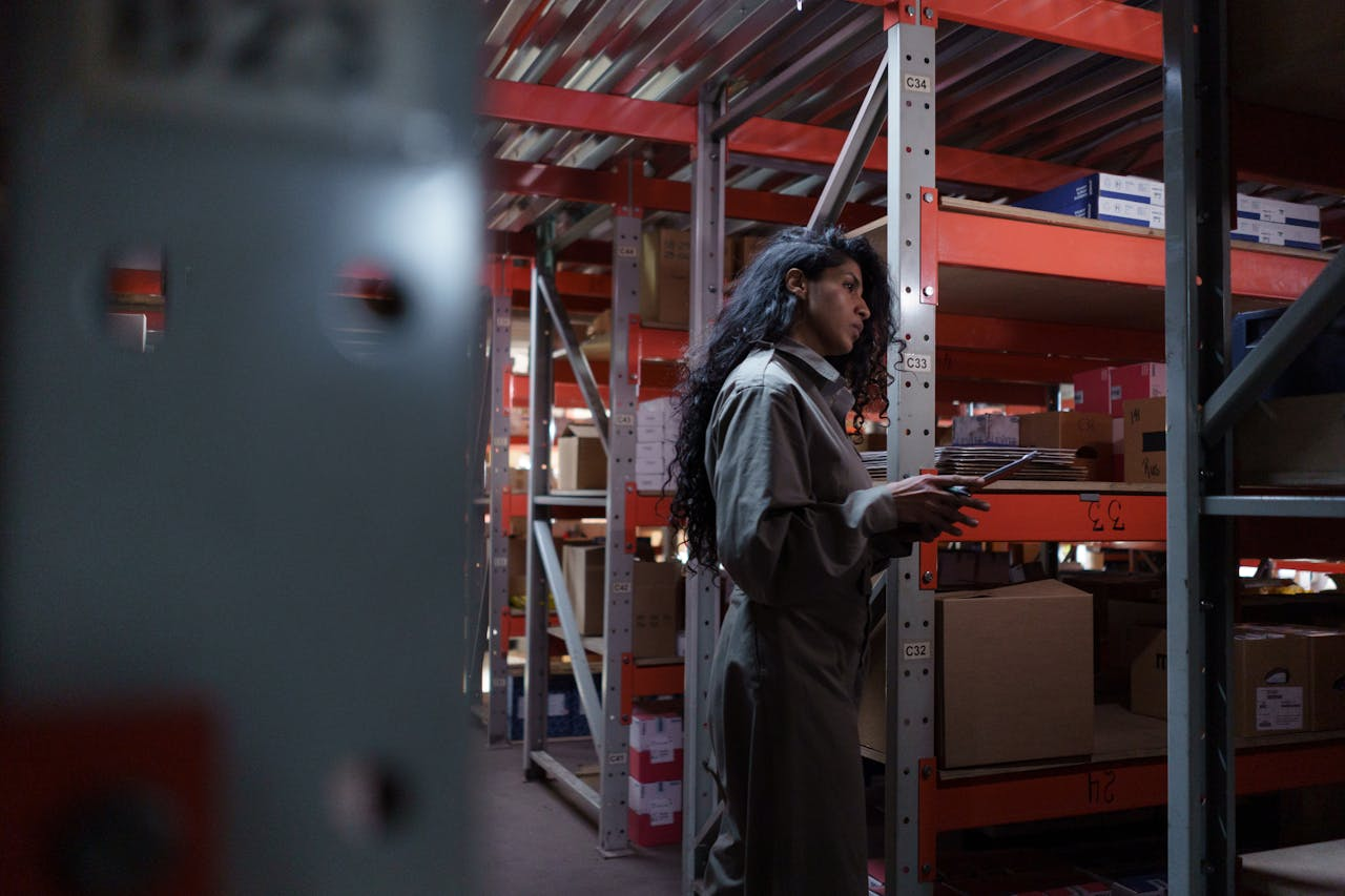 services-01 An adult woman in uniform checking inventory in a warehouse aisle.